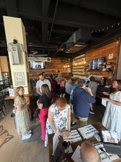 Attendees filling out activity sheets at a check-in table while others mingle by the bar at Work The Room at the Raccoon Taproom