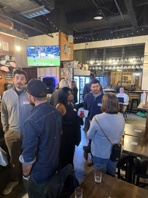 Attendees mingling near the bar with a ballgame on TV at Work The Room in Collingswood