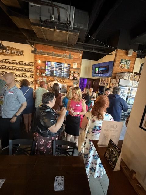 A crowded room of attendees with name tags talking in small groups under the Raccoon Taproom sign