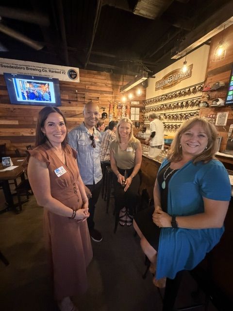 Four attendees smiling for the camera beside the bar, with the Raccoon Taproom mug wall behind them