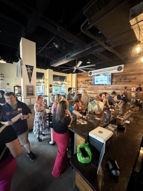 Attendees lined up along the bar and talking in pairs at the Raccoon Taproom