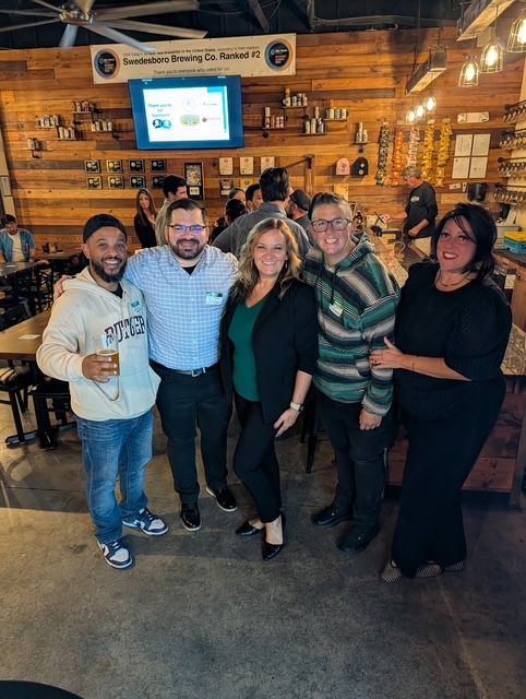 Five attendees posing for a group photo under the Swedesboro Brewing Co. banner at Work The Room in Collingswood
